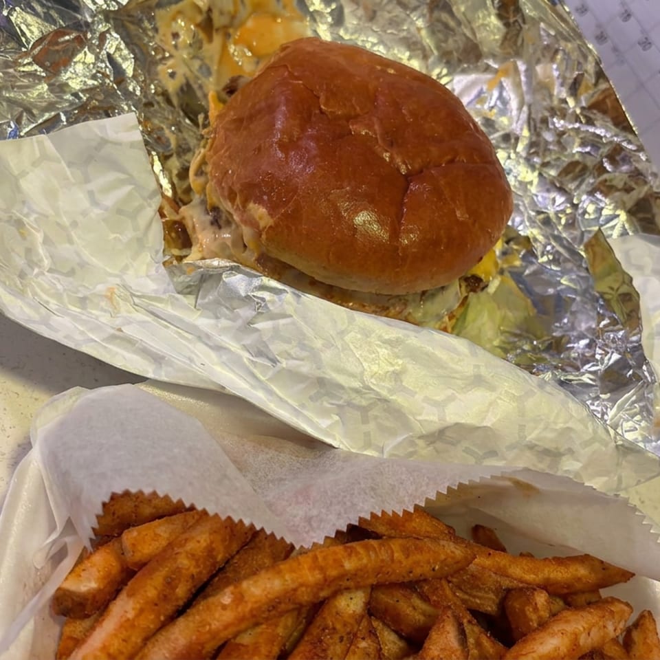 Cheeseburger wrapped in foil with a tray of seasoned fries on a countertop.