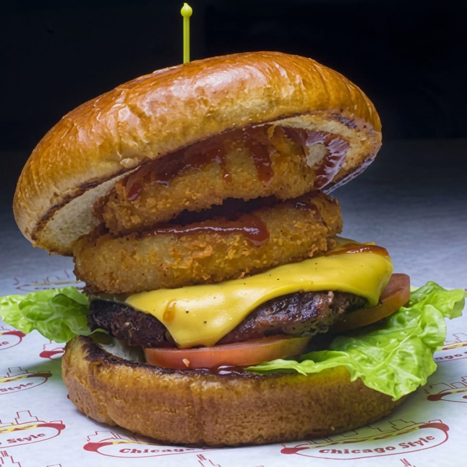 Double-patty burger with melted cheese, lettuce, tomato, crispy fried toppings, sauce, and a toasted bun on Chicago Style paper.